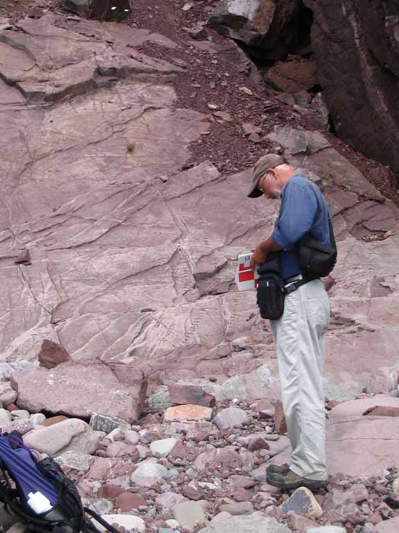 Photographie couleur d’un homme debout, bloc-note à la main, devant des rochers roses