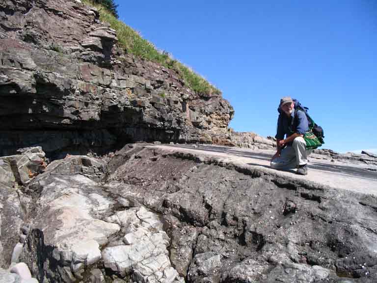 Photographie couleur d’un homme au pied d’une falaise, un genou sur la roche