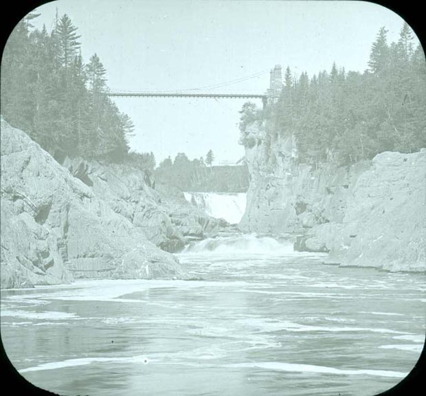 Image noir et blanc de la rivière, des rives rocheuses et, en arrière-plan, d’un pont suspendu