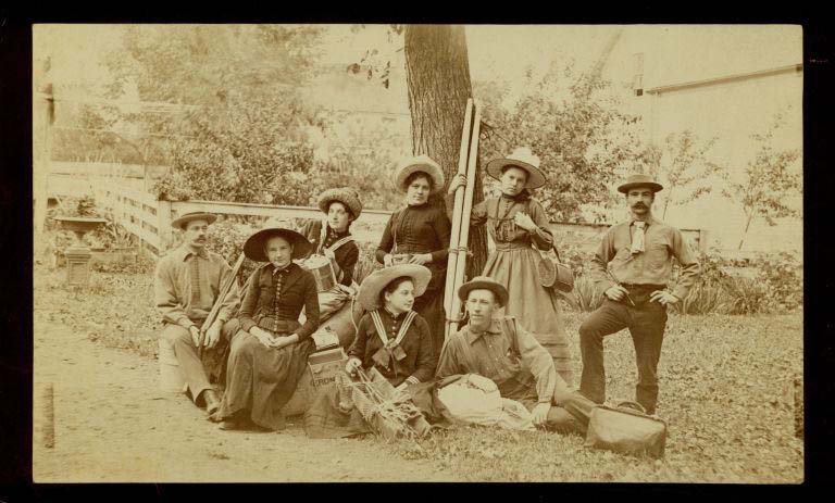 Photographie noir et blanc de cinq femmes et trois hommes devant un arbre
